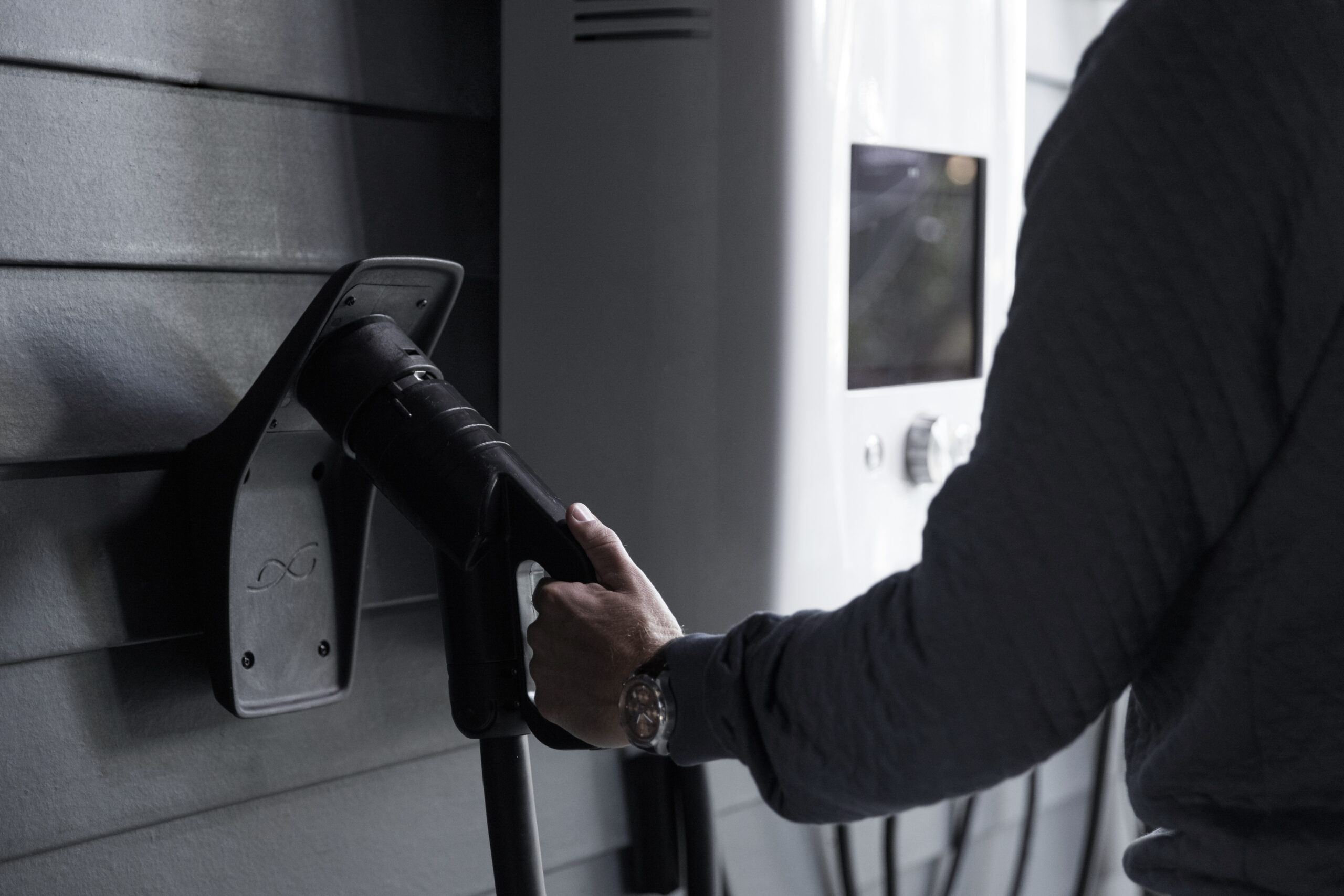 Man charging his electric car at a home charging station with a wall-mounted control device.